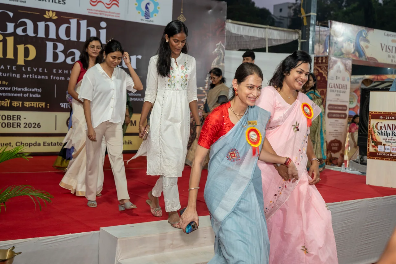 Women in saris and patterned outfits walk down from the Gandhi Shilp Bazaar stage.